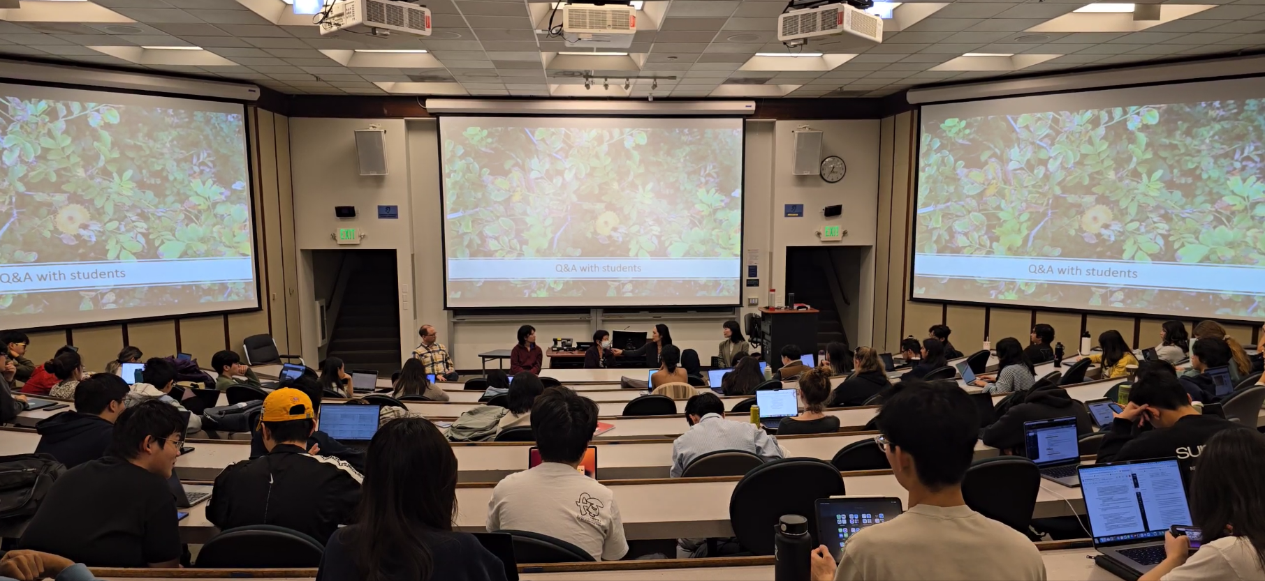 A view from the back of the lecture hall of students facing the four panelists.