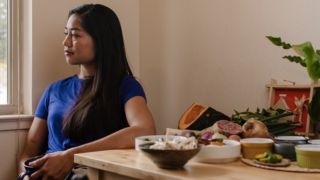 Woman sits beside table of food staring thoughtfully